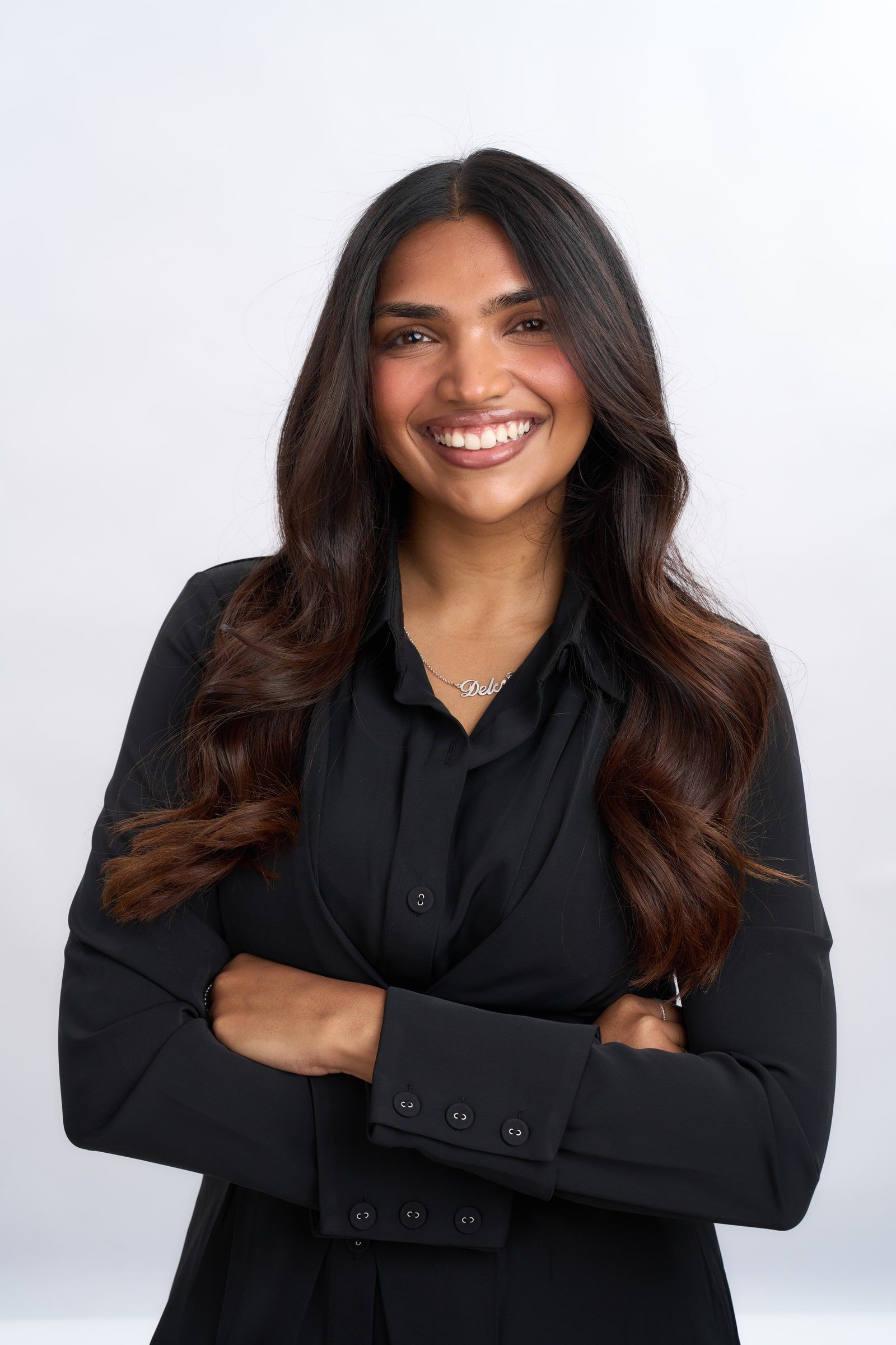 Delcy Pandya in black with her arms crossed, smiling, wearing a necklace that spells Delcy